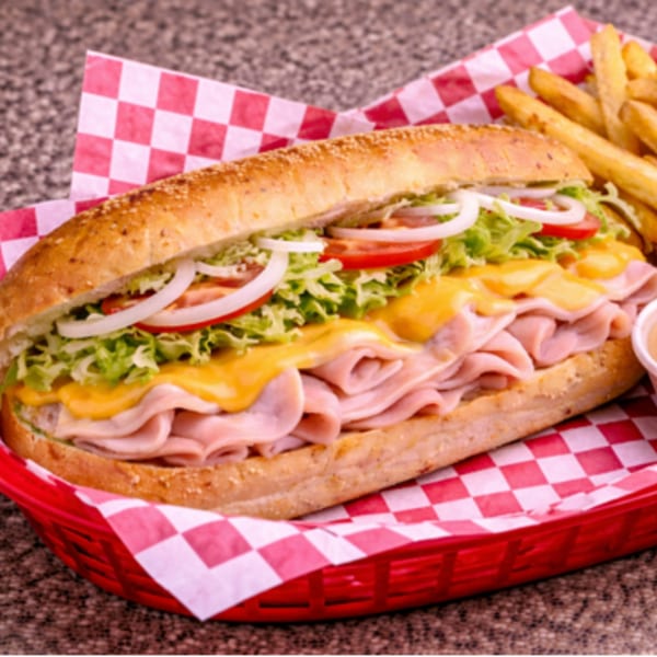 A large ham and cheese sub sandwich with lettuce, tomatoes, and onions, served with fries.