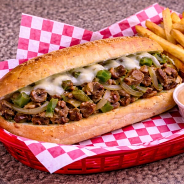 Cheesesteak sandwich with melted cheese, steak, onions, and green peppers, served with fries and dipping sauce.