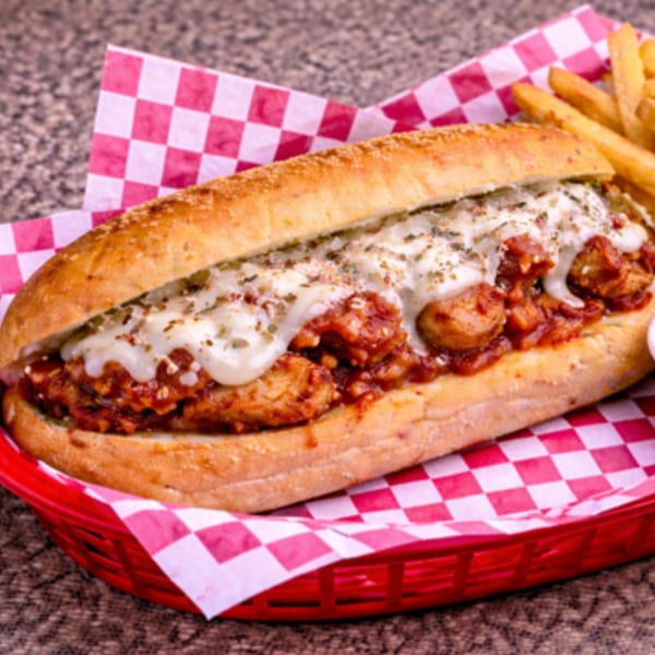 A chicken parmesan sub sandwich with melted cheese and sauce, served with fries in a red basket.
