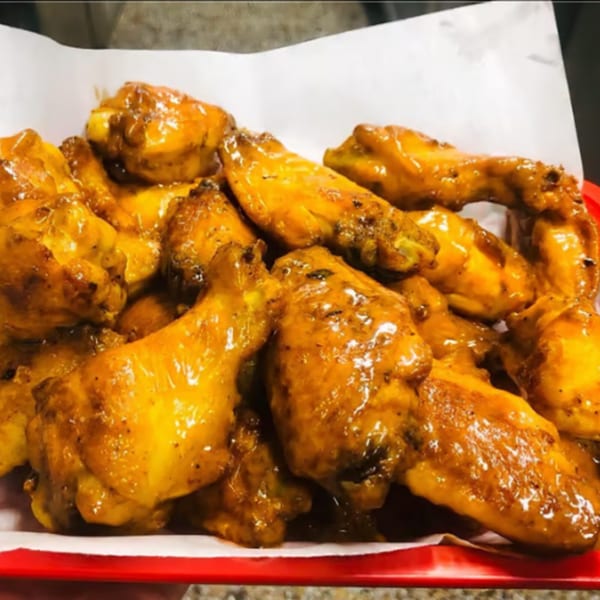 A close-up of a pile of golden-brown chicken wings coated in a glossy sauce, served on white paper in a red basket.